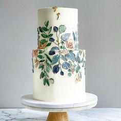 a three tiered cake decorated with flowers and leaves on a marble platter against a gray wall