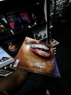 a person holding up a magazine in front of a book shelf filled with dvds and movies