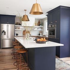 a large kitchen with blue cabinets and gold pendant lights over the island countertop, along with stools