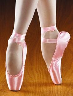 a woman in pink ballet shoes standing on a wooden floor