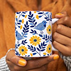 a woman holding a coffee mug with yellow and blue flowers on it