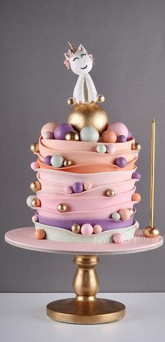 a multi layer cake decorated with pink, purple and gold icing on a stand