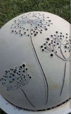 a white vase sitting on top of a grass covered field with flowers painted on it