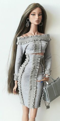 a barbie doll wearing a dress and holding a handbag in her right hand while standing next to a white wall