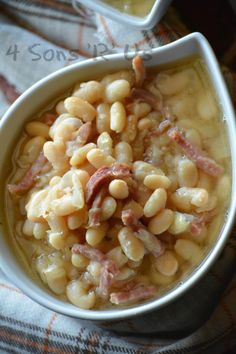 two bowls filled with beans and ham on top of a cloth covered table next to a cup of soup