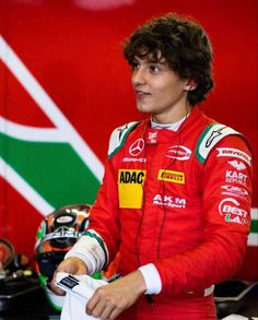 a man in a red racing suit standing next to a helmet on a race track