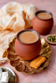 two cups of coffee on a plate with crackers and other food items around them