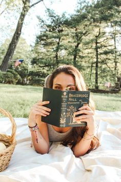 a woman laying on top of a blanket holding a book in front of her face