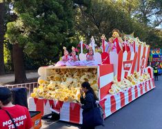 Moomba parade float shaped like big striped tubs of popcorn, tipping over and spilling their contents. Kids sitting on top of the float wave to the crowd. Buttery popcorn sculpted out of foam. Popcorn Parade Float Ideas, Circus Theme Parade Float, Floats For Parade, Halloween Parade Float, Parade Float Ideas, Popcorn Buckets, Homecoming 2024, Popcorn Stand