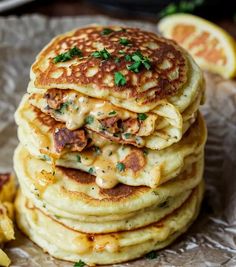 a stack of pancakes covered in cheese and parsley next to sliced lemon wedges