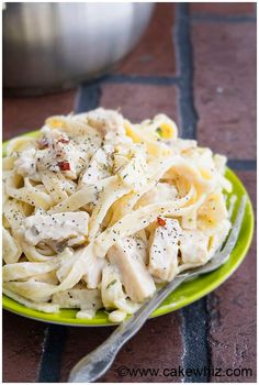 a green plate topped with pasta covered in chicken and parmesan cheese on top of a table