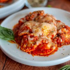 a white plate topped with lasagna covered in sauce and cheese on top of a wooden table