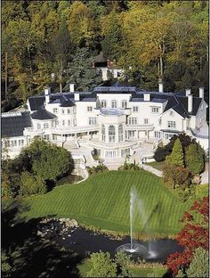 an aerial view of a large white mansion with a fountain in the foreground and trees surrounding it