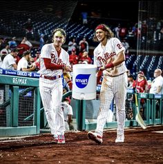 two baseball players are walking towards the dugout with buckets in their hands as people watch