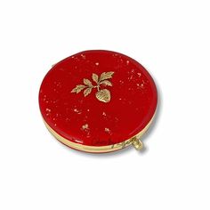 a small red box with gold trimmings and a strawberry on the front, sitting on a white surface