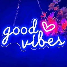 a neon sign that says good vibes hanging from a chain with flowers in the background