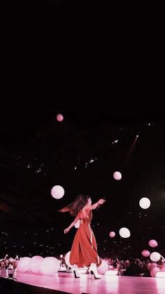 a woman in a red dress is walking on a stage with balloons floating above her