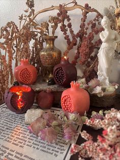 pomegranates and flowers are on display in front of a book with an angel figurine