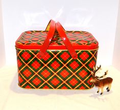 a small toy deer standing next to a red and green plaid suitcase