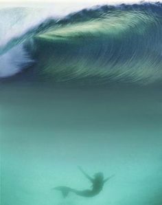 a person swimming in the ocean with a large wave behind them and their shadow on the water