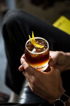 a person holding a drink with orange peels on the rim in their left hand