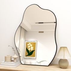 a mirror sitting on top of a wooden table next to a lamp and vase with flowers in it