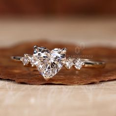 a heart shaped diamond ring sitting on top of a piece of wood next to a leaf