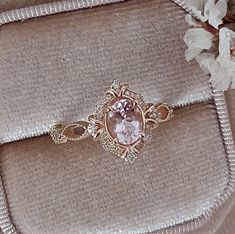 a pink diamond ring sitting on top of a cushion