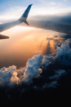 the wing of an airplane as it flies through the sky with clouds and sunbeams