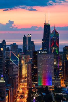 the city skyline is lit up at night with colorful lights and skyscrapers in the background