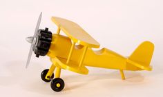 a yellow toy airplane with black wheels on a white background