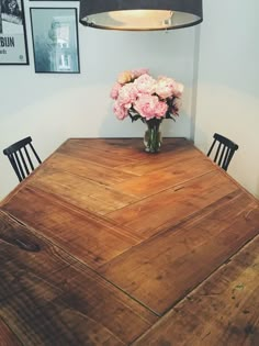 a wooden table with flowers in a vase sitting on it's end, under a light fixture