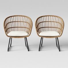 two rattan chairs with white cushions and black metal legs, one is facing the other