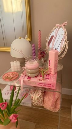 a table topped with lots of pink items next to a mirror and potted plant