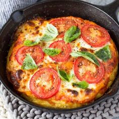 a pizza with tomatoes and basil in a cast iron skillet on top of a table