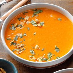 a bowl of carrot soup on a table with other bowls and spoons next to it