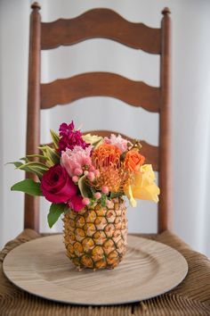 a pineapple vase filled with flowers on top of a wooden chair