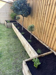 two wooden planters filled with dirt next to a fenced in yard and trees