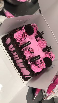 a pink and black cake with oreo cookies on top is in a white box