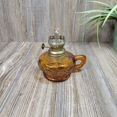 an old glass teapot with a crown on top sits on a wooden table next to a potted plant