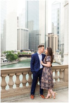 a man and woman standing next to each other on a bridge in front of tall buildings