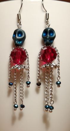 pair of earrings with red and blue beads hanging from hooks on white plated surface