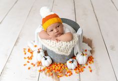 a baby is sitting in a bucket with candy corn on the floor and wearing a knitted hat