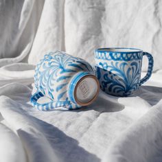 two blue and white coffee cups sitting on top of a white cloth covered tablecloth