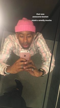 a man looking at his cell phone while wearing a pink knitted hat and striped shirt