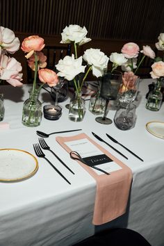 the table is set with pink and white flowers in glass vases, silverware, and napkins