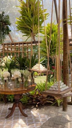 an outdoor area with hanging plants and flowers in vases on wooden tables, surrounded by greenery