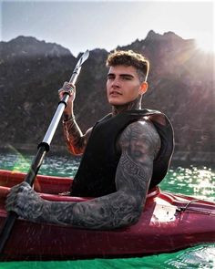 a man with tattoos on his arm sitting in a kayak and holding a fishing pole