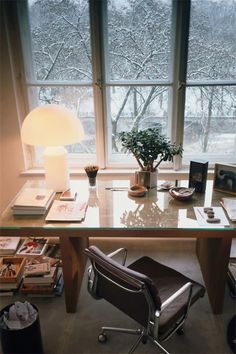 a desk with a chair, lamp and pictures on it in front of a window