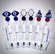 six pens with different designs and shapes in front of a clear display case on a white surface